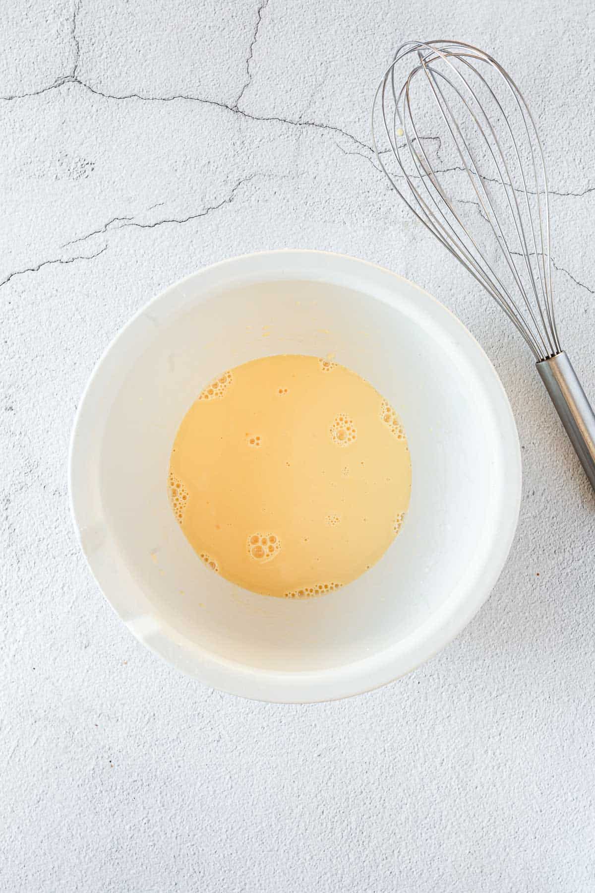 A white bowl with a whisk next to it, preparing gluten free blueberry chocolate chip muffins.