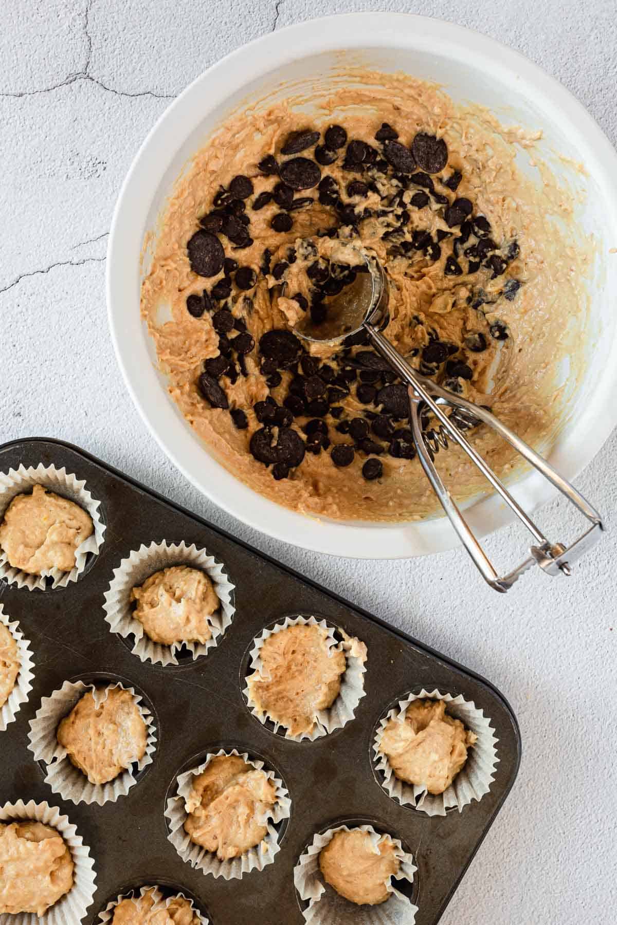 Gluten-free peanut butter cupcakes with chocolate chips in a muffin tin, mixed with a whisk.