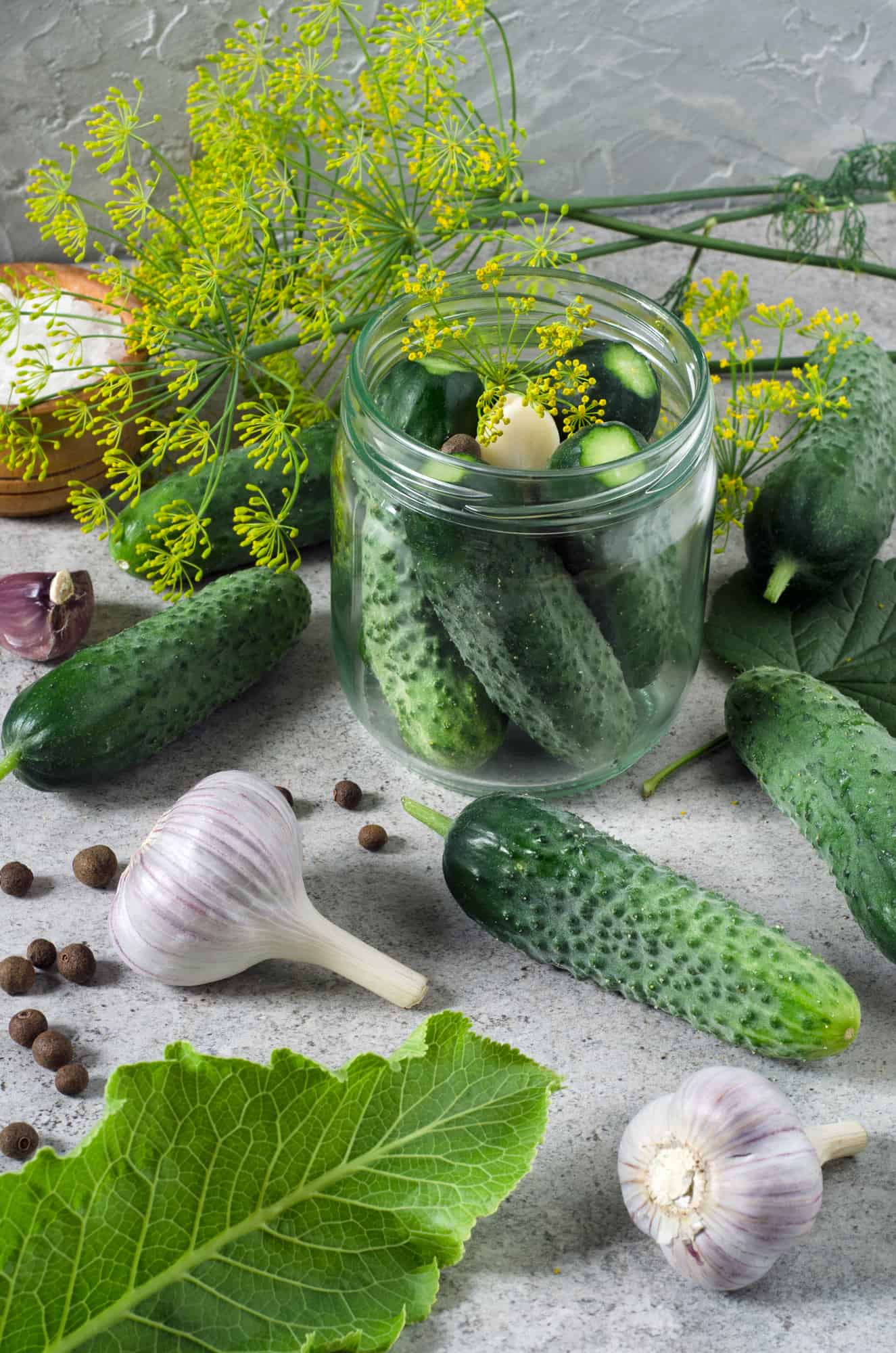 A glass jar filled with cucumbers, garlic, and herbs brimming with deliciously tangy fermented pickles.