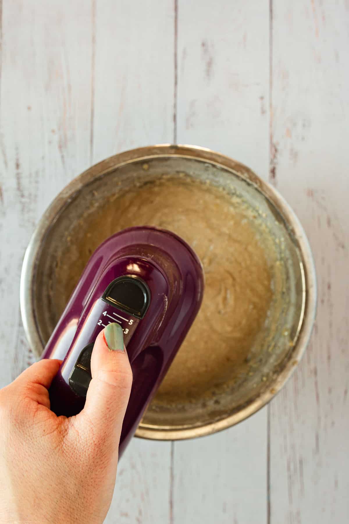 A person is using a hand held electric mixer to make muffins.