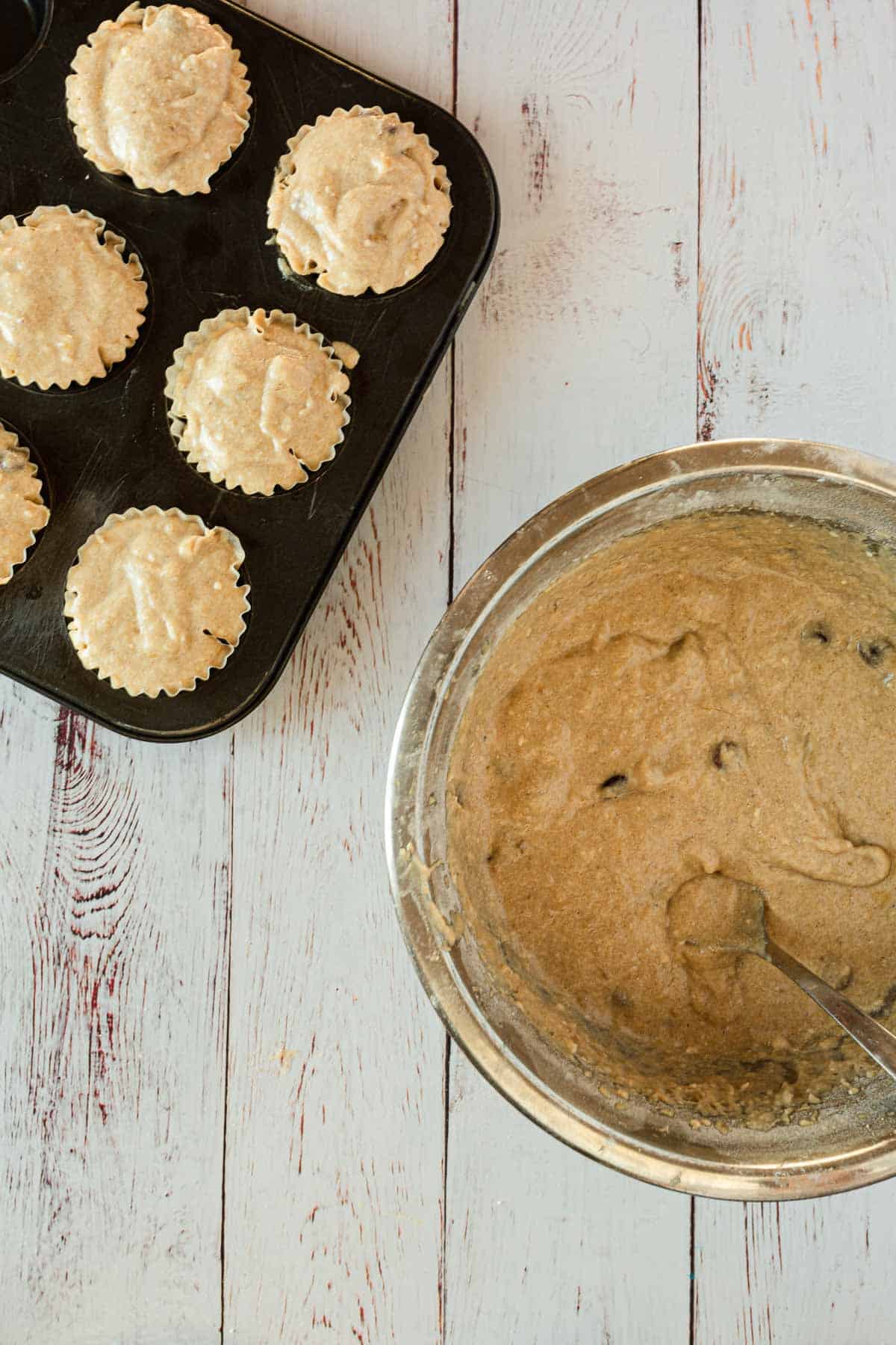 Muffins in a pan next to a bowl of batter.