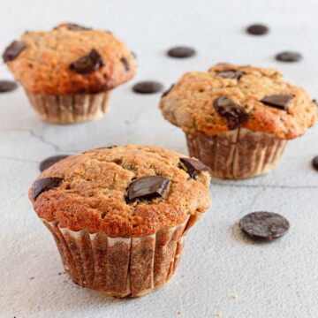 Three chocolate chip muffins on a white surface.