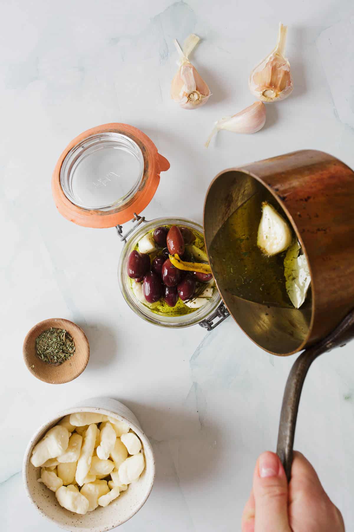 A person pouring olive oil into a jar with other ingredients.