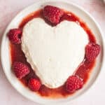 A heart shaped dessert with raspberries and cream on a plate.