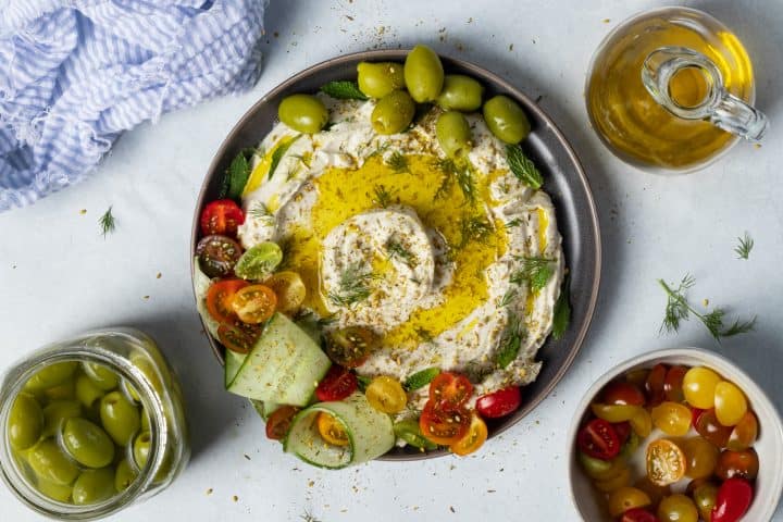 A plate of middle eastern dips with olives and a glass of oil.