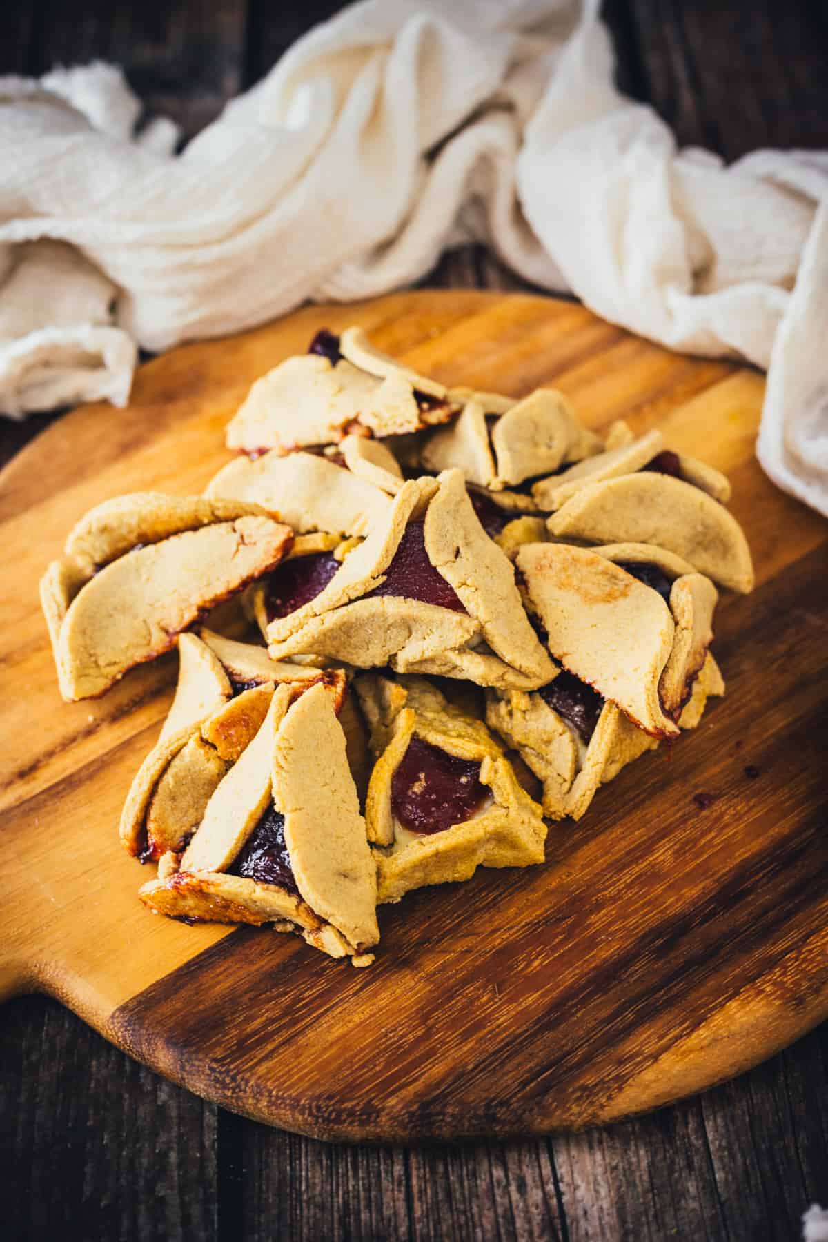 Slices of a fruity Guava Cheese Hamantaschen with a golden crust served on a wooden cutting board, with a white cloth in the background.