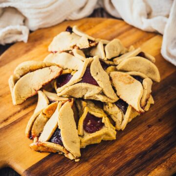 A pile of freshly baked jam-filled hamantaschen on a wooden cutting board.