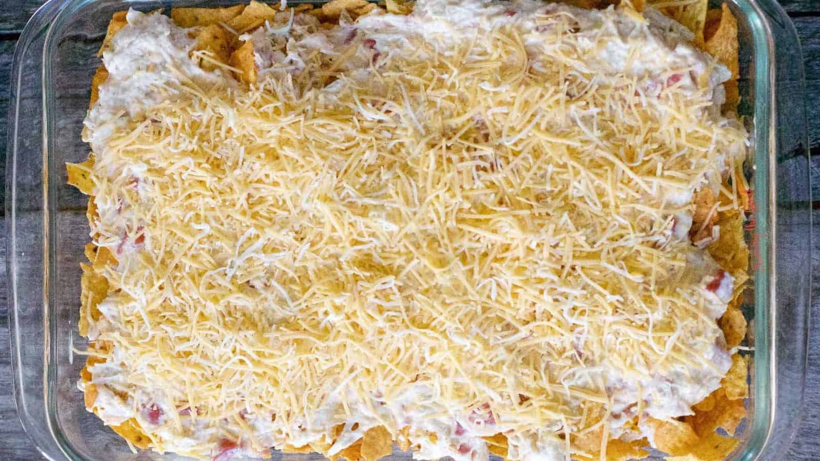 A glass baking dish filled with layered nachos topped with melted shredded cheese and Auto Draft.