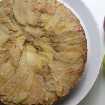 A slice of Grandma's apple cake on a plate with apples next to it.