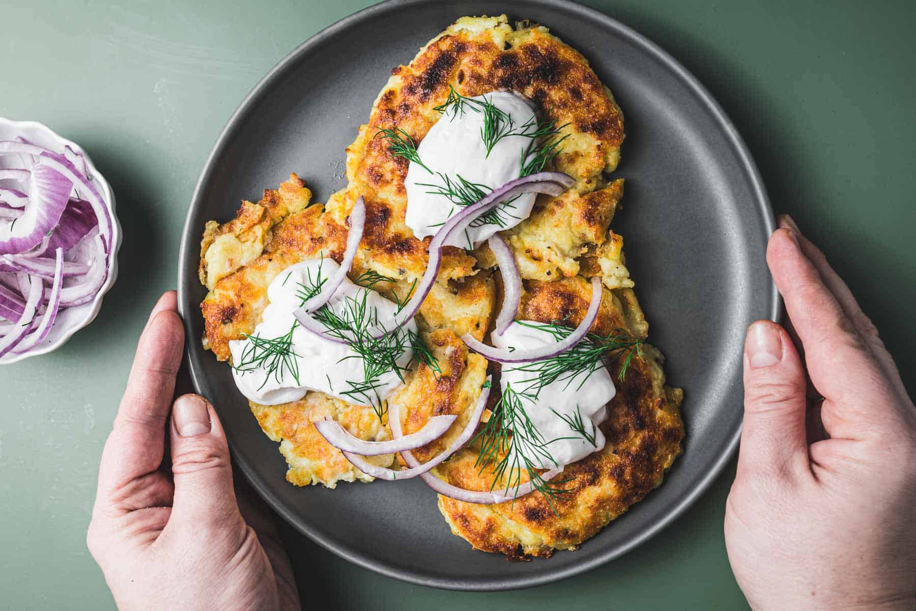 A plate of potato pancakes with onions and sour cream.