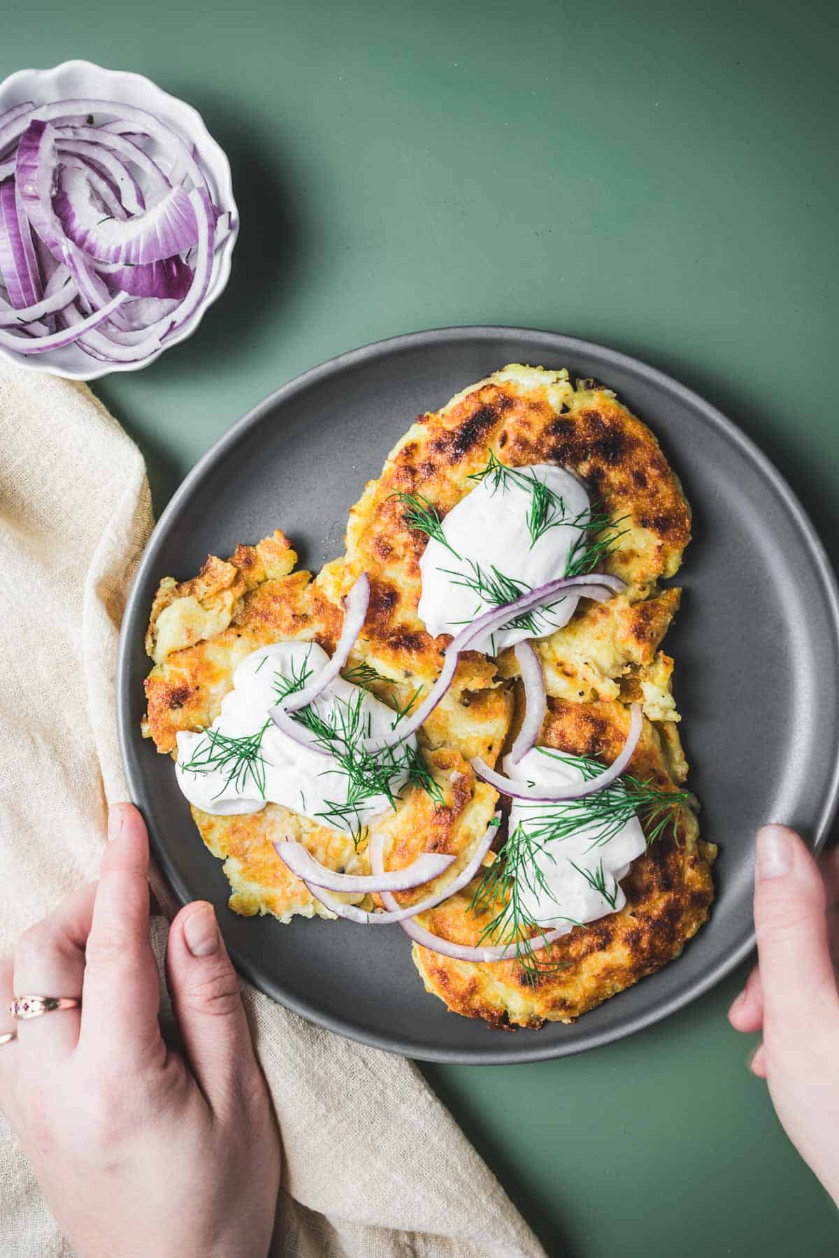 mashed potato pancakes with sour cream and onions on a plate.