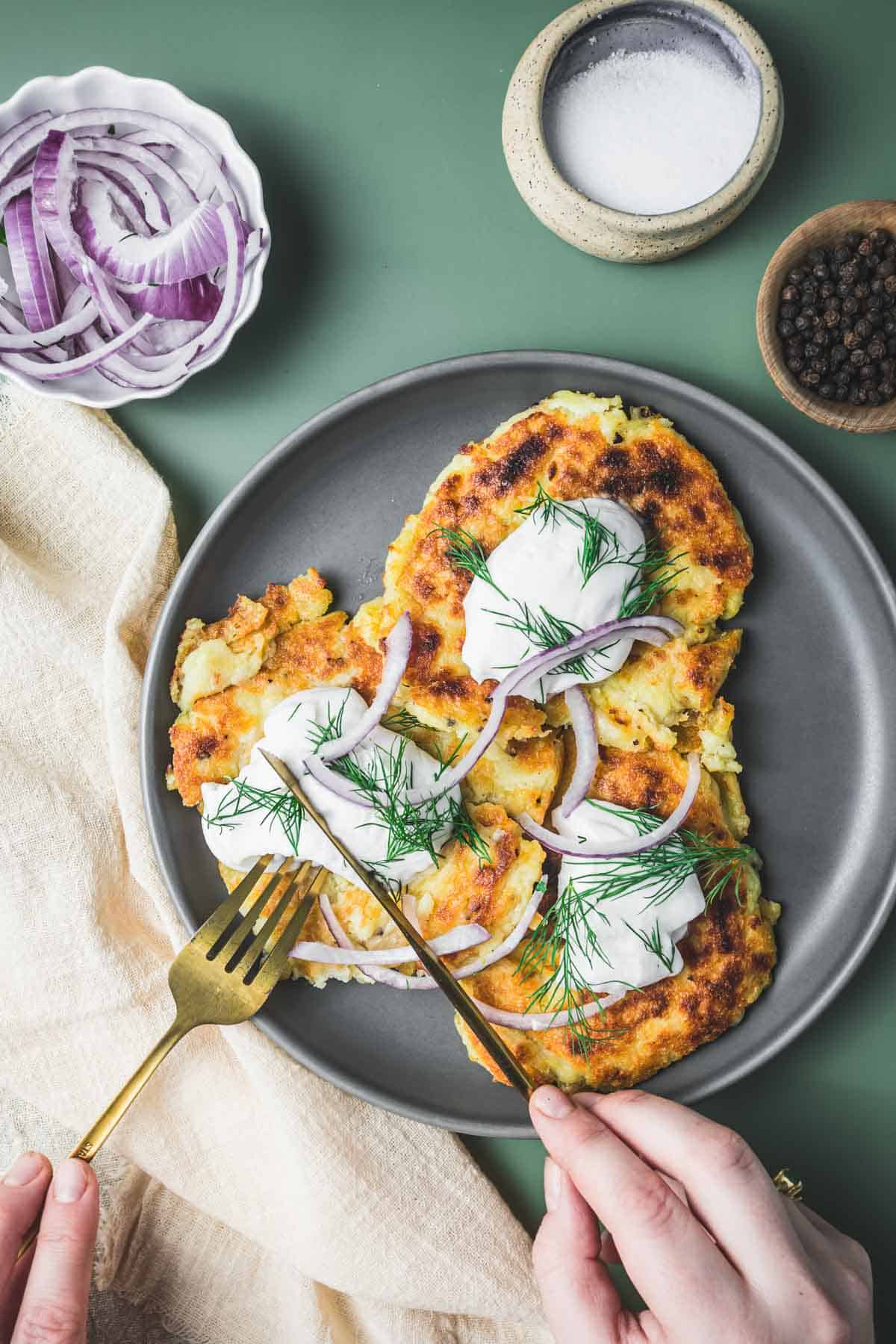 A plate of potato pancakes with onions and sour cream.