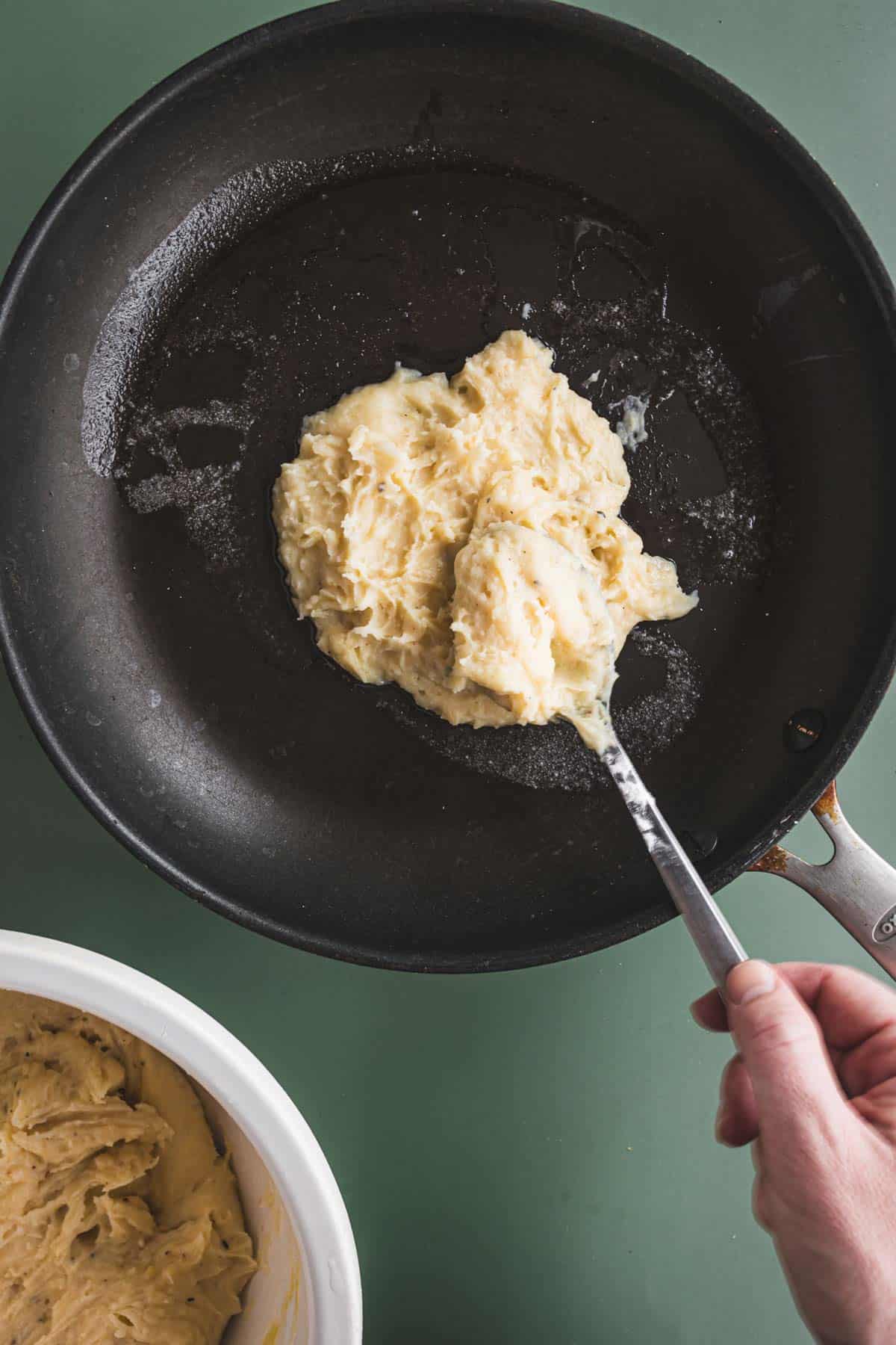 A person using a spatula to place a batter in a frying pan.