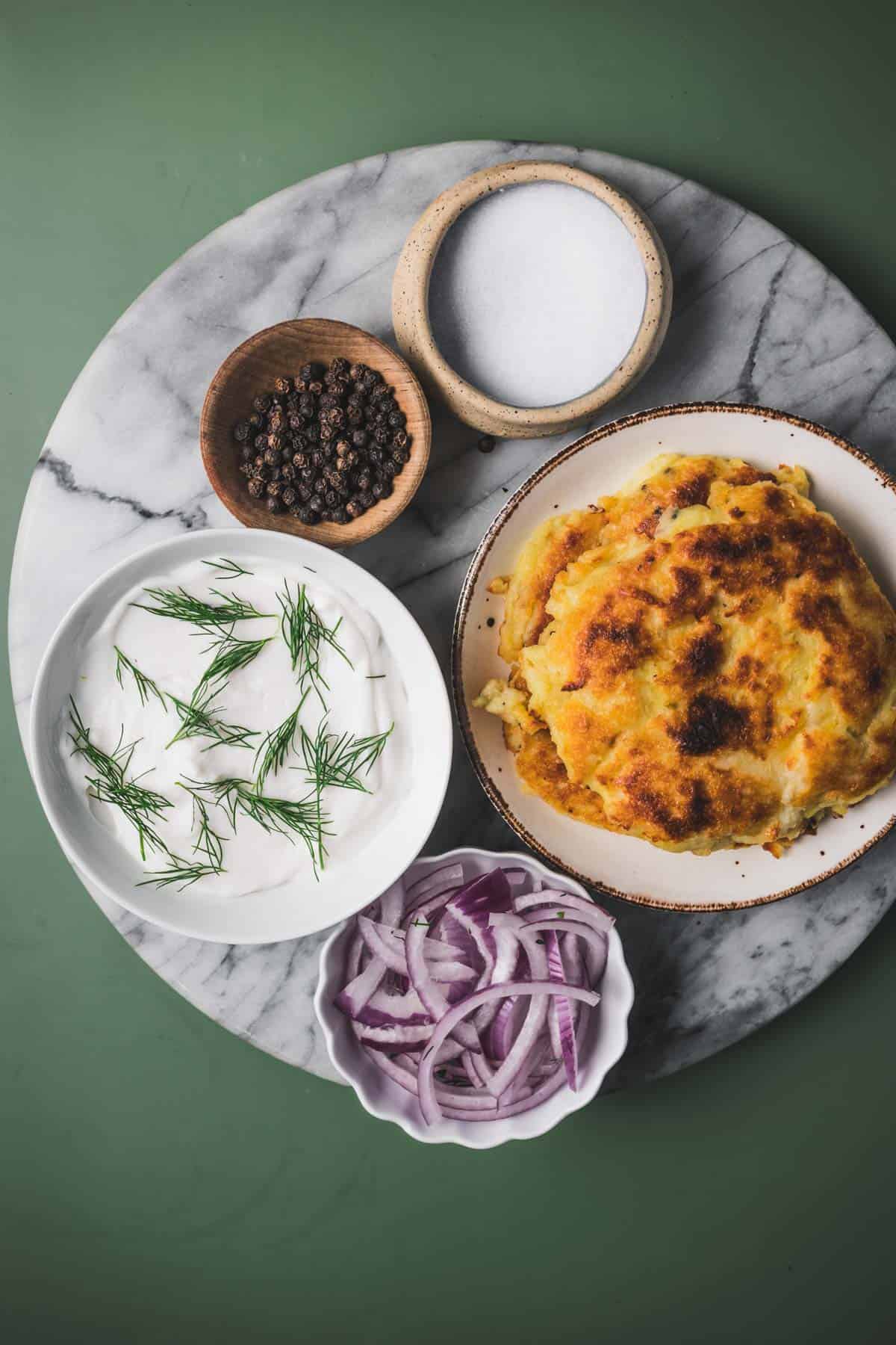 A plate of latkes with onions and other toppings on a marble table.