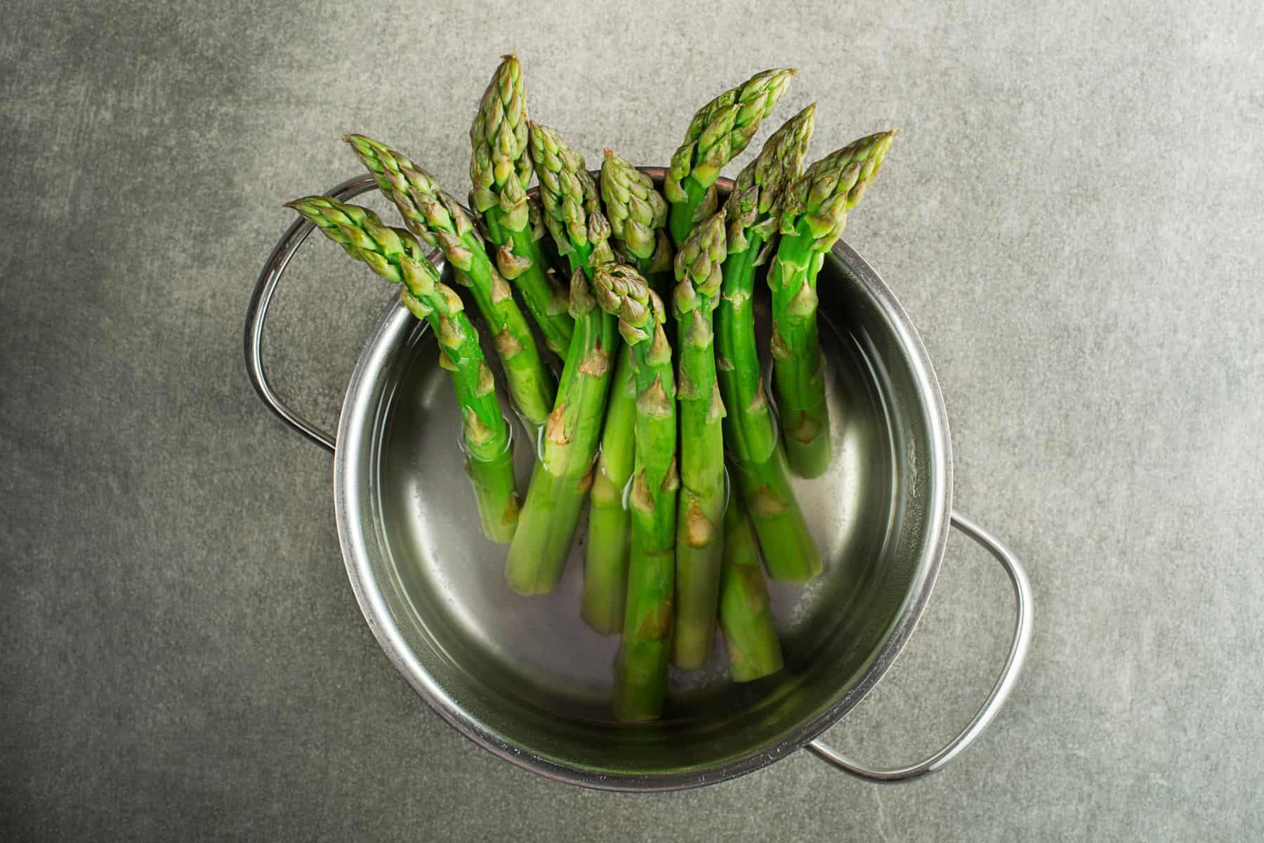 Discover how to cook asparagus like a pro with a bunch of fresh spears standing upright in a metal colander.