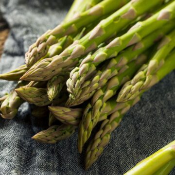 A bundle of fresh green asparagus spears on a textured cloth, ready for cooking asparagus.