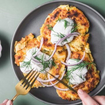 A person is holding a plate of pancakes with onions and dill.