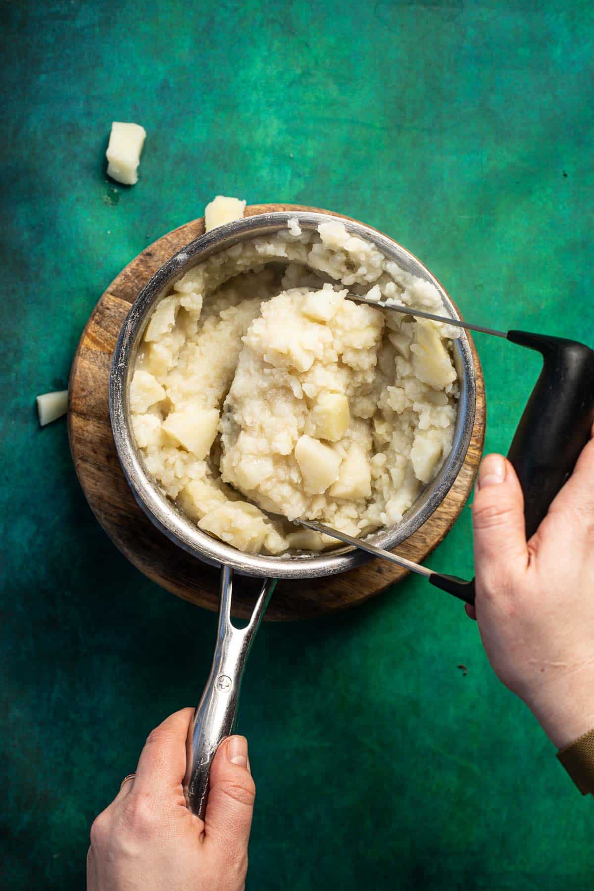 A person mixing potatoes in a pan with a spatula.