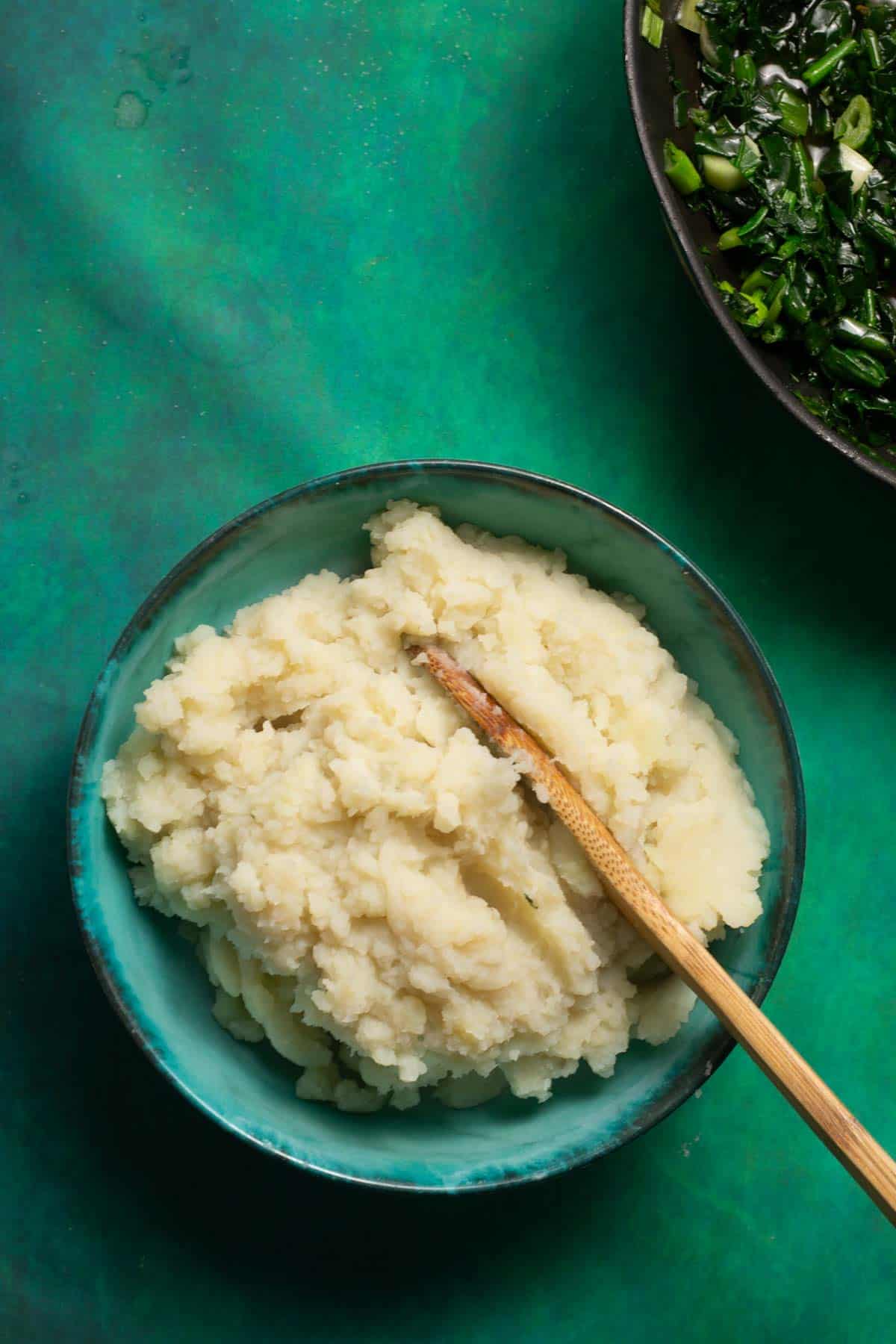 A bowl of mashed potatoes and a bowl of greens.
