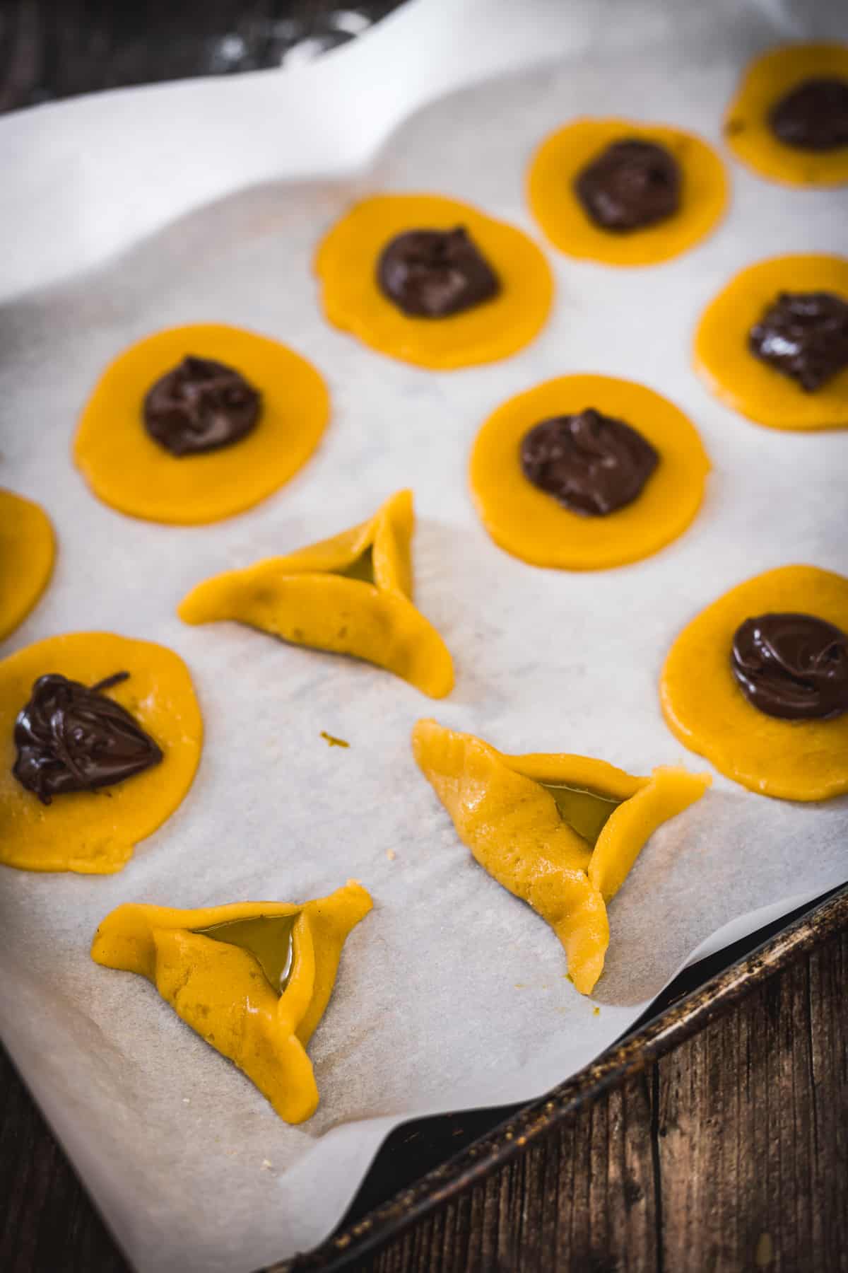 Unbaked Rose Pistachio Hamantaschen on parchment paper, with some shaped into crescents and others awaiting folding.