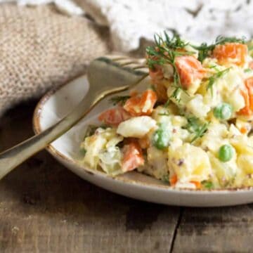 A bowl of carrot and potato salad on a wooden table.