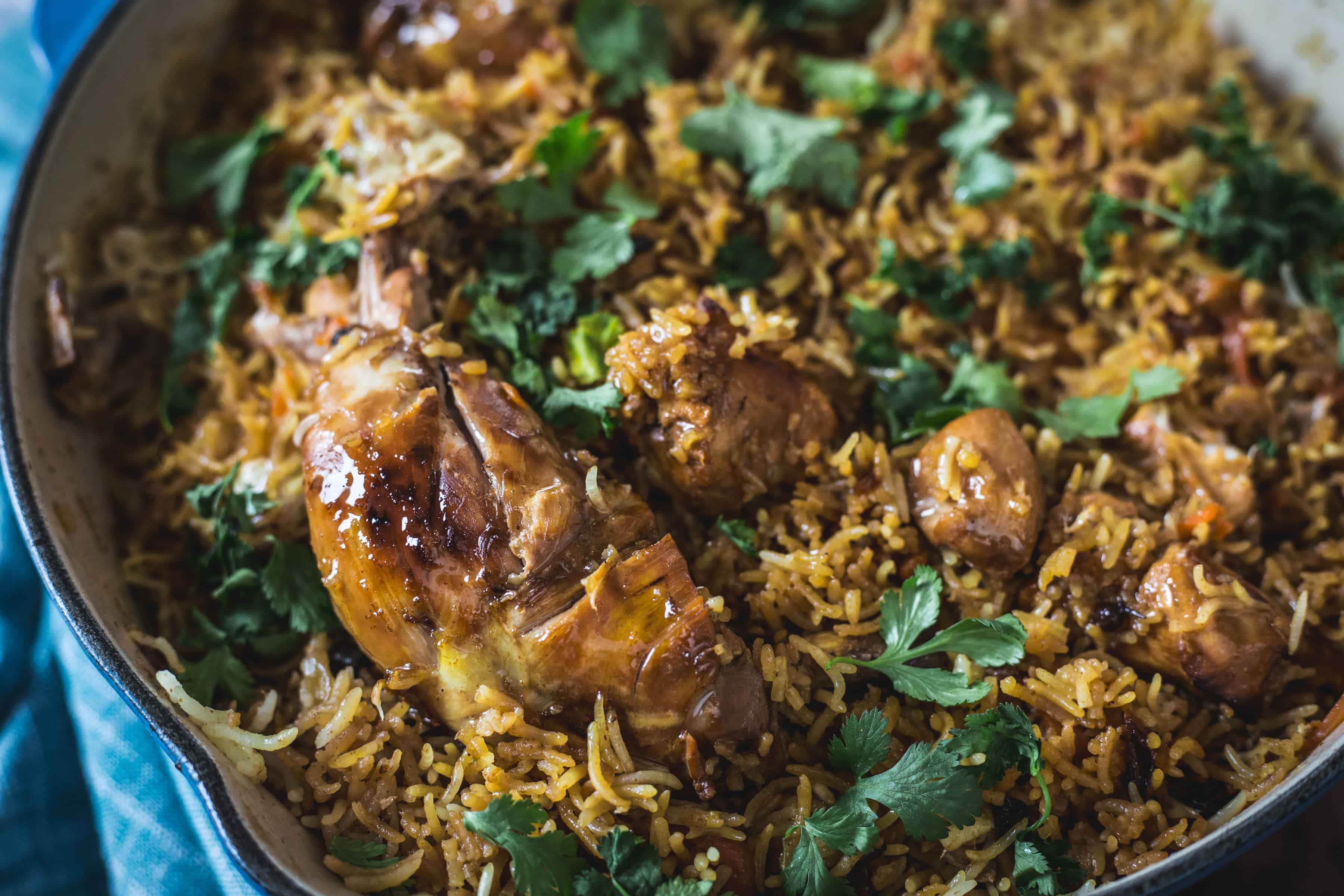 Chicken plov in a skillet on a blue tablecloth.