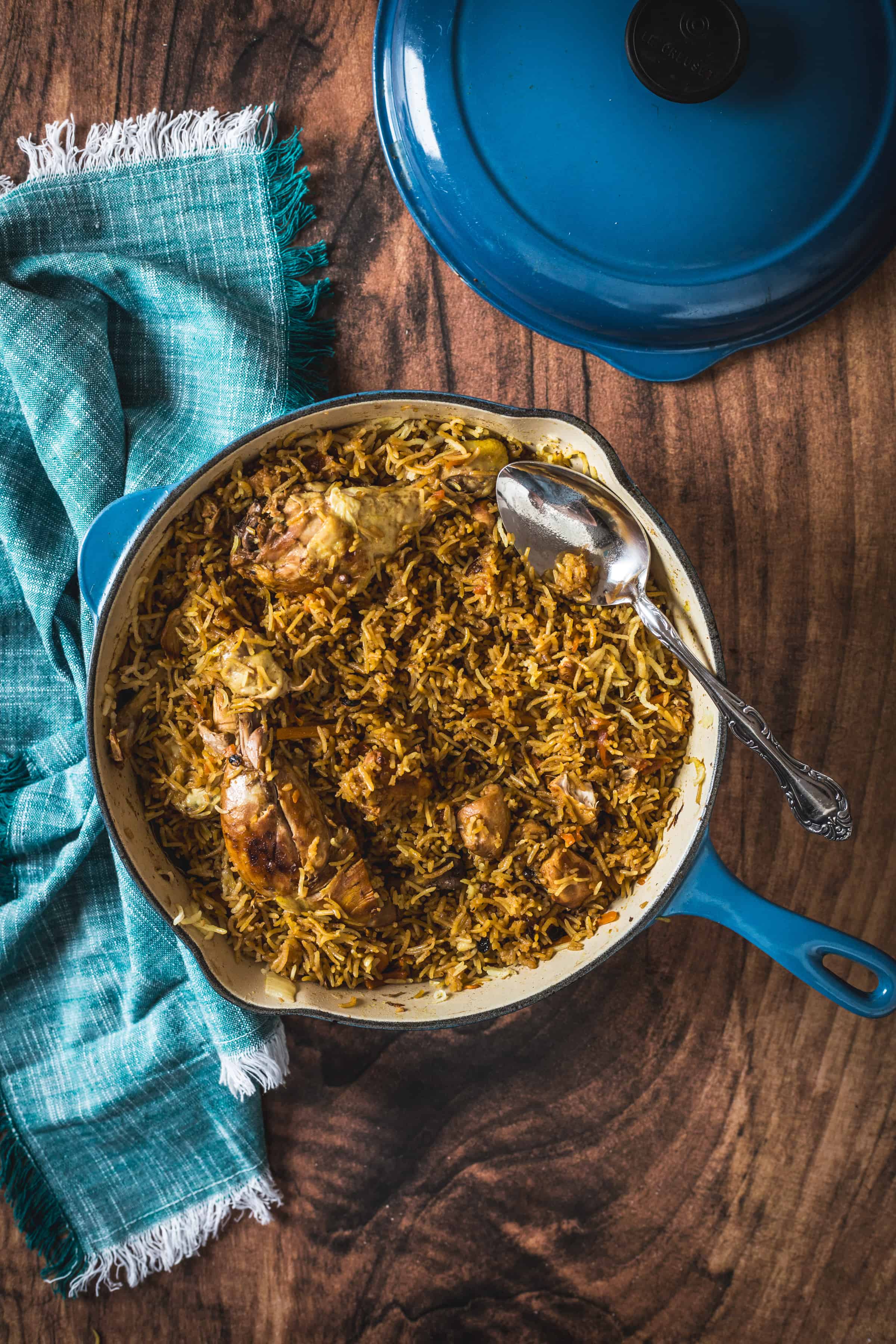 Chicken plov in a blue pot on a wooden table.