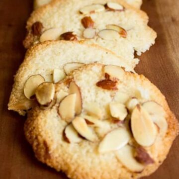 Thin, crisp almond tuile cookies topped with sliced almonds, on a wooden serving board.