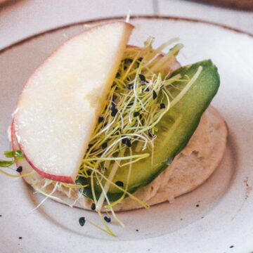 A plate with a slice of apple, avocado, and sprouts served on a creamy spread makes for a quick dinner recipe.