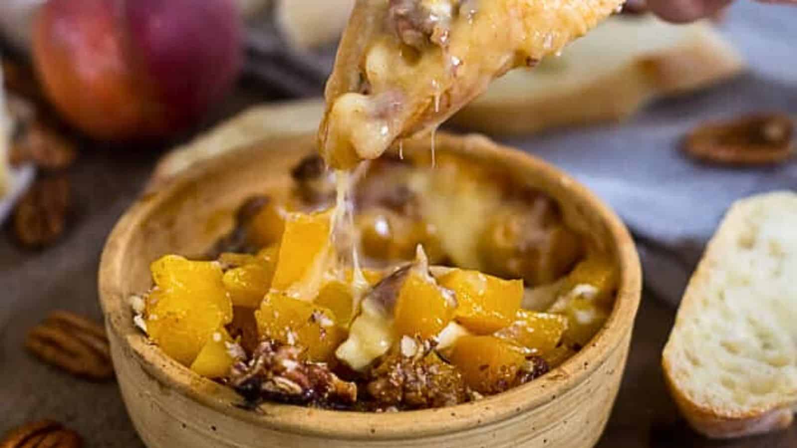 A piece of bread being dipped into a 30-minute baked cheese dish with nuts and fruit pieces.