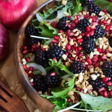 A quick mixed berry salad with pomegranate seeds, blackberries, and chopped nuts served in a wooden bowl, accompanied by a whole pomegranate and apple, with wooden serving utensils
