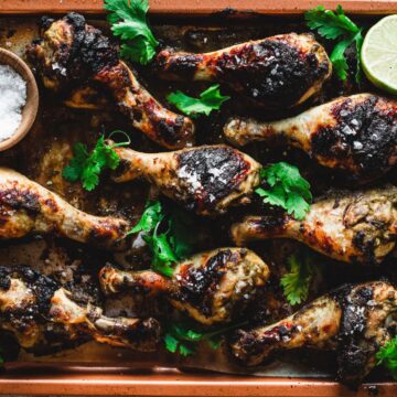 Cooked chicken drumsticks garnished with fresh cilantro and slices of lime, served on a rectangular baking tray with a small wooden bowl of salt on the side. Explore Grandma's secret chicken recipes.