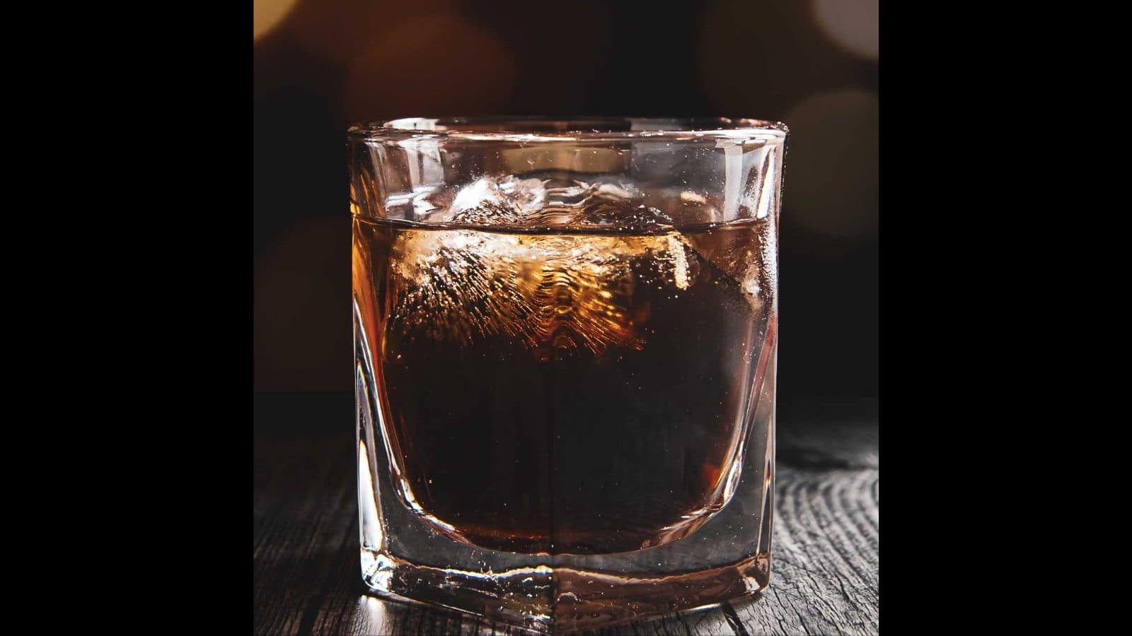 A glass of whiskey with ice on a wooden surface, illuminated by soft background lighting that creates a warm, inviting glow, reminiscent of drinks at grandma's house.