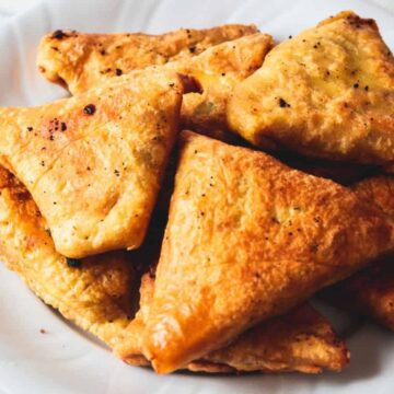 Golden-brown triangular samosas on a white plate.