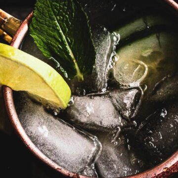 Close-up of a moscow mule cocktail in a copper mug, garnished with a slice of lime and a sprig of mint, served with ice.