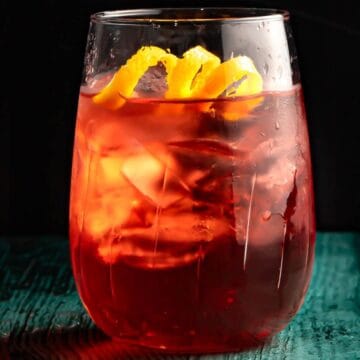 A glass of iced tea with a slice of lemon on top, set against a dark backdrop with light highlighting the beverage's vibrant red color and condensation on the glass.