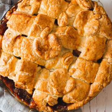 A freshly baked apple pie with a lattice crust and decorative pastry leaves, straight from Grandma's secret recipes, sits on a wooden table.