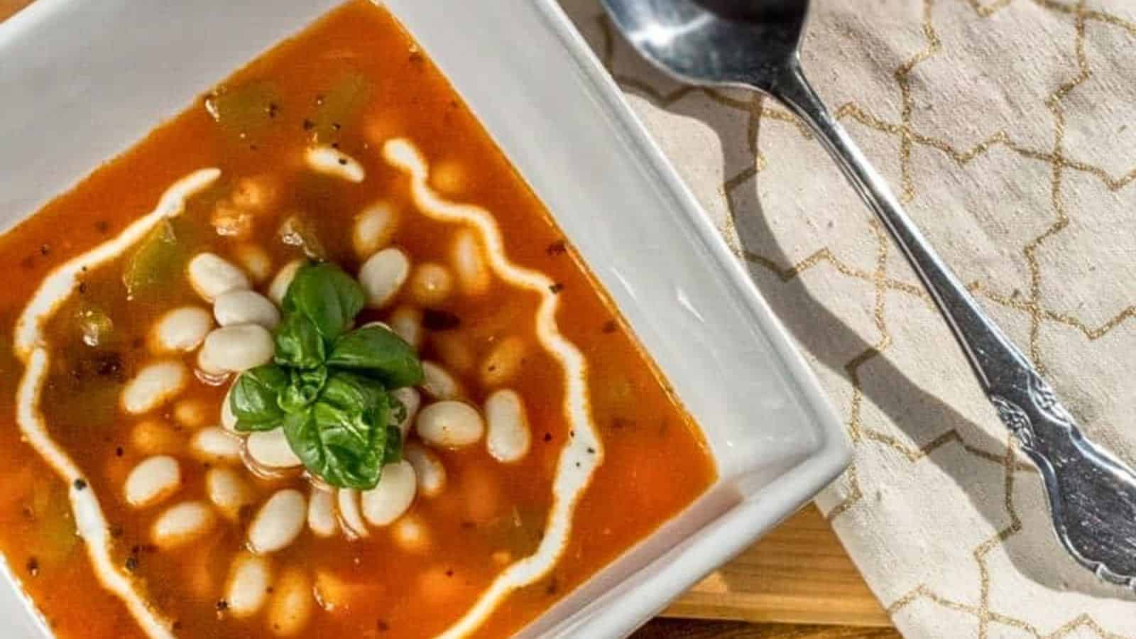 A white bowl of soup with a spoon and basil.