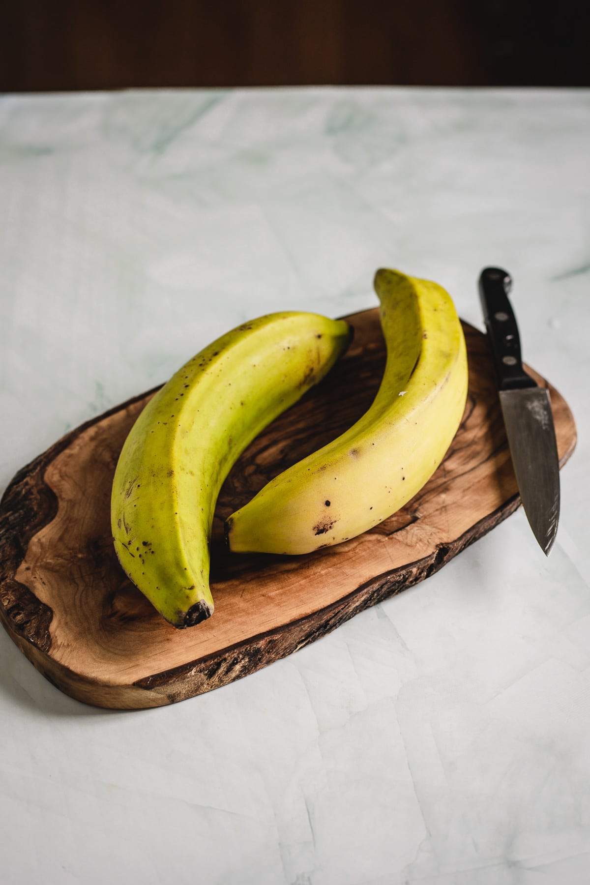 Two traditional Colombian Patacones on a wooden cutting board next to a knife.