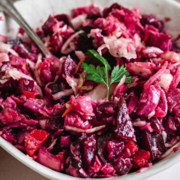 A bowl of Grandma's beetroot salad garnished with a sprig of parsley, with a fork resting in it, placed on a table next to a cloth napkin.
