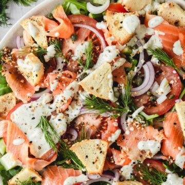 A vibrant salad with smoked salmon slices, fresh dill, tomatoes, onions, and crispbread, drizzled with a creamy dressing, served quickly on a white platter.