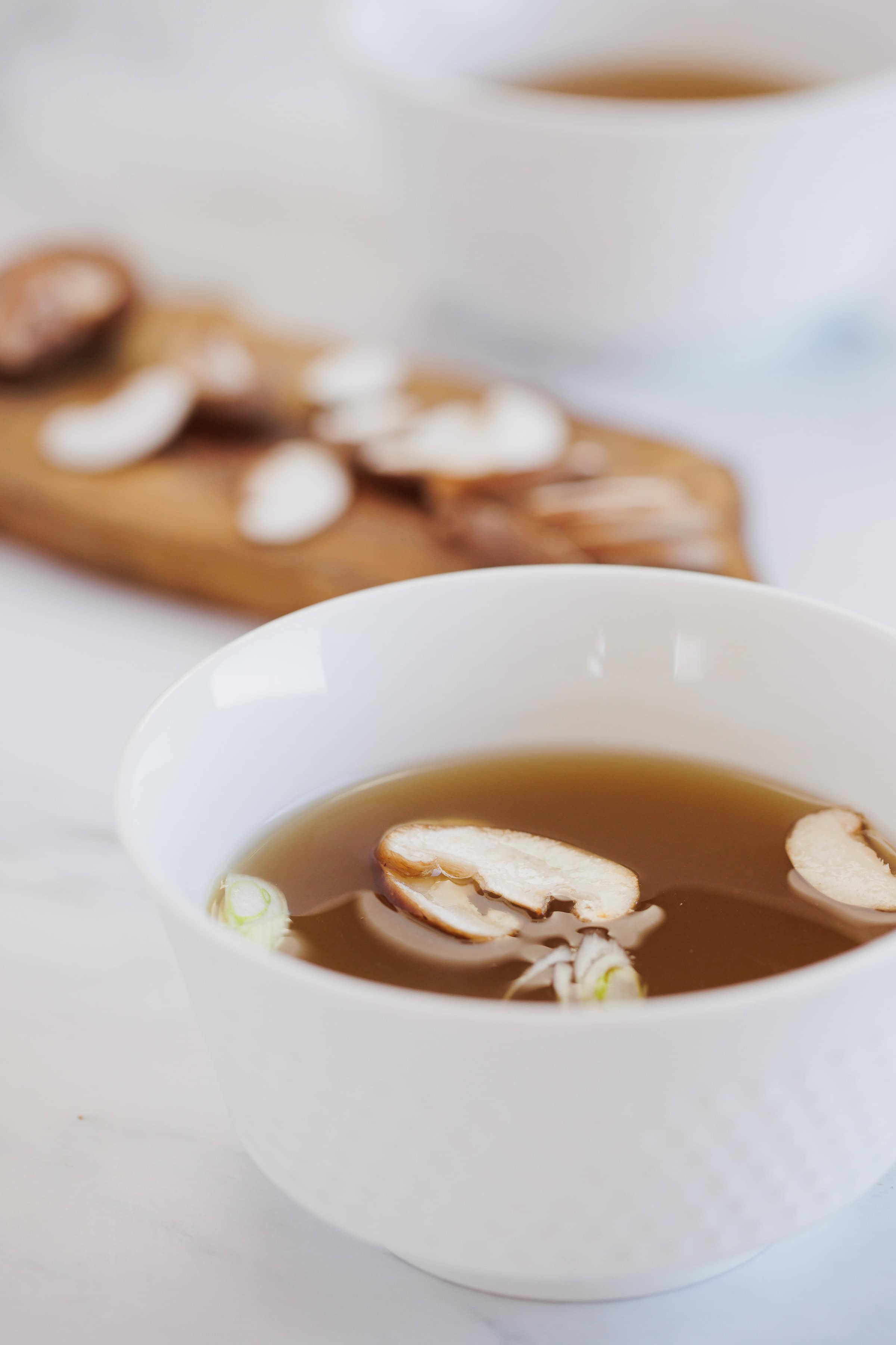 mushroom broth in a small white bowl topped with fresh sliced mushrooms.