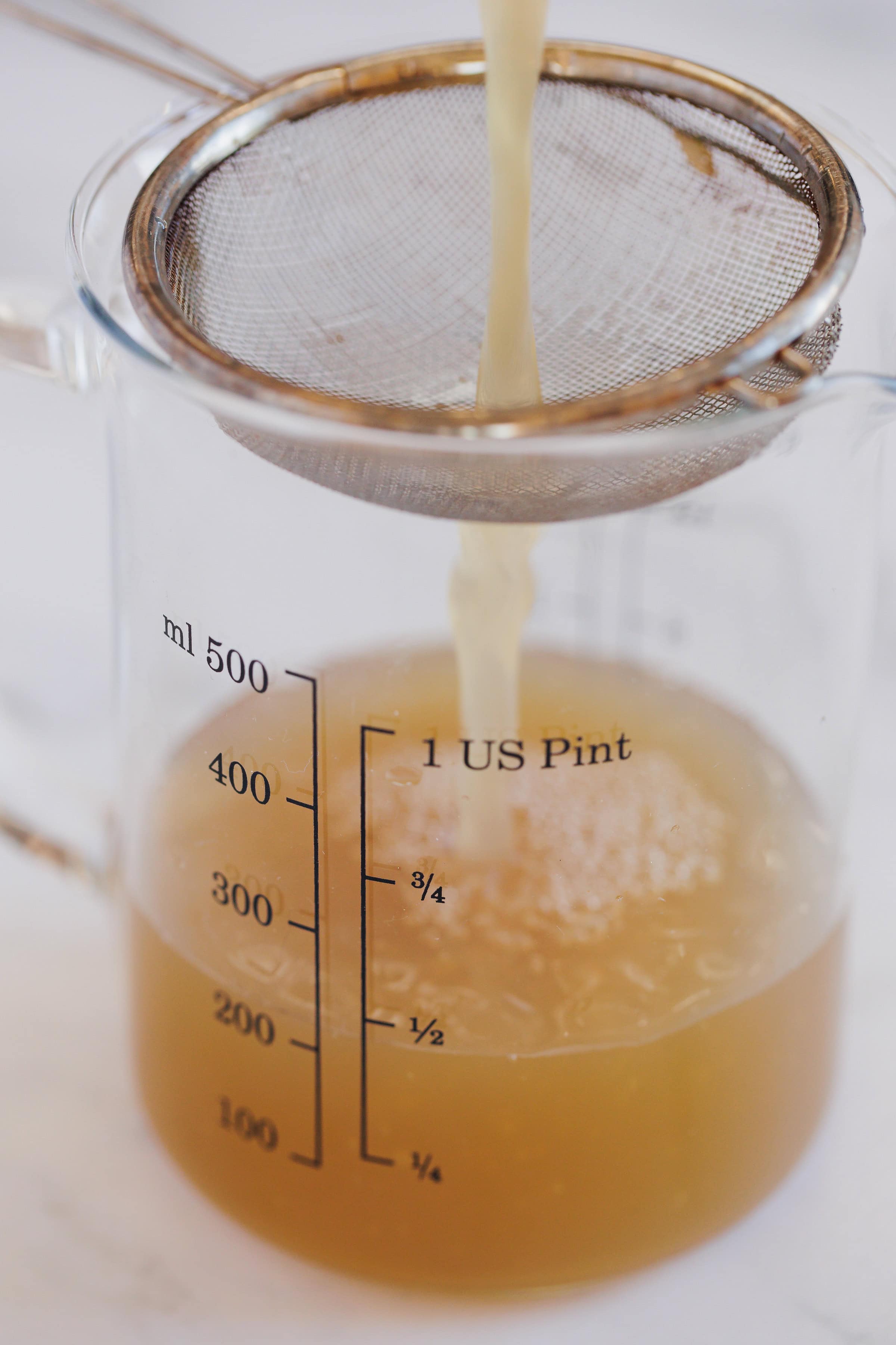 shiitake mushroom broth being poured through a fine mesh strainer into a measuring cup.