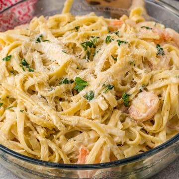 A glass bowl of creamy shrimp alfredo pasta topped with grated parmesan cheese and chopped parsley, placed on a kitchen counter with utensils nearby, featured in our weekly food guide.