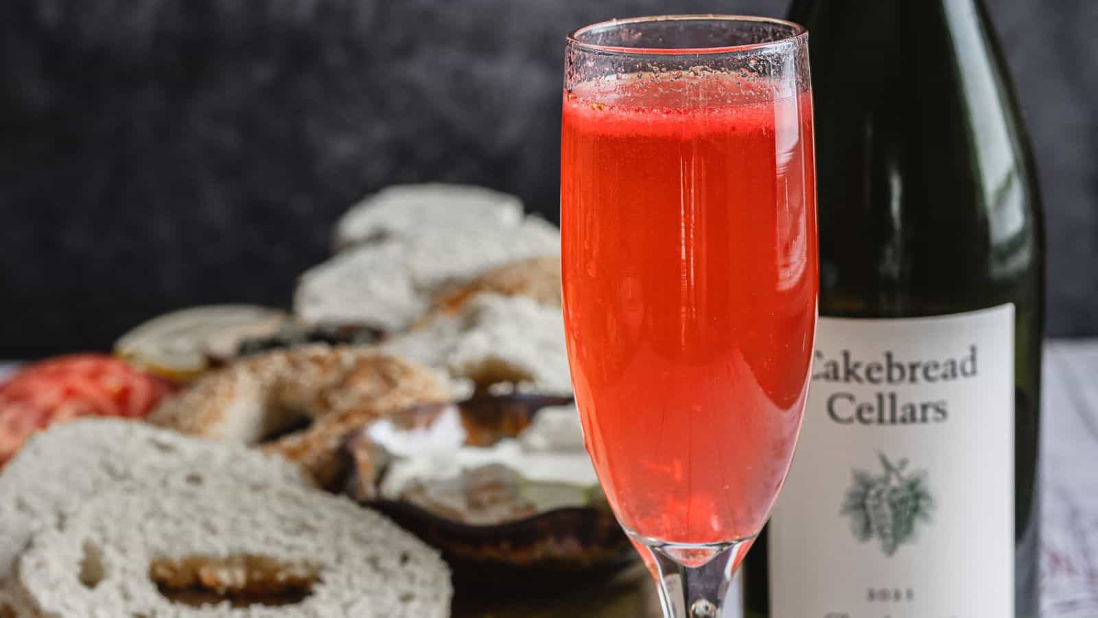 One glass with bagels and wine bottle in background.