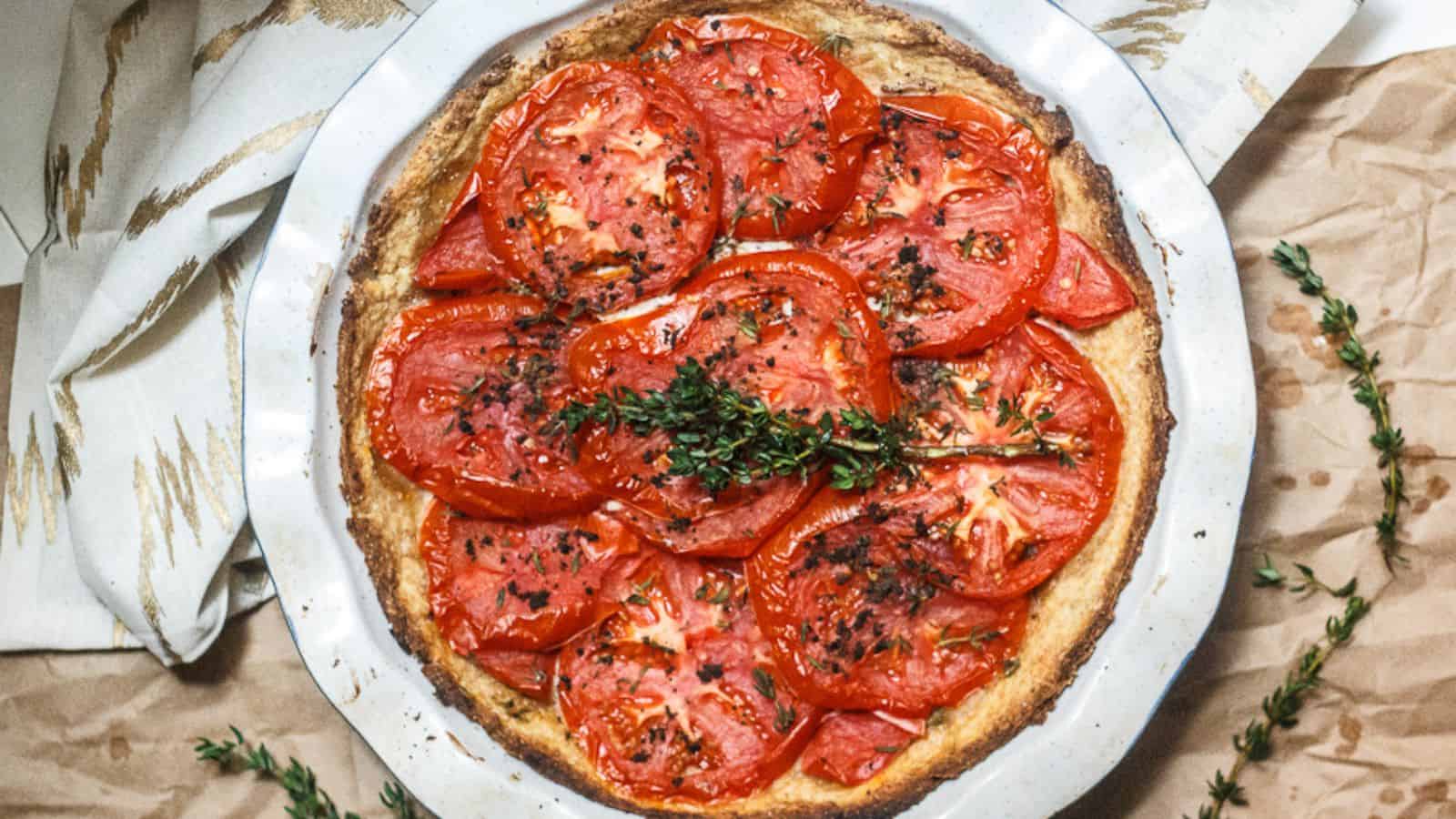 A freshly baked tomato tart, following one of Grandma's recipes, is garnished with herbs and served in a round, white baking dish on a parchment-lined surface. The tomatoes are vibrant and arranged in