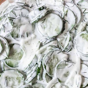 A glass bowl filled with quick cucumber salad, featuring thinly sliced cucumbers and fresh dill, mixed with a creamy white dressing.