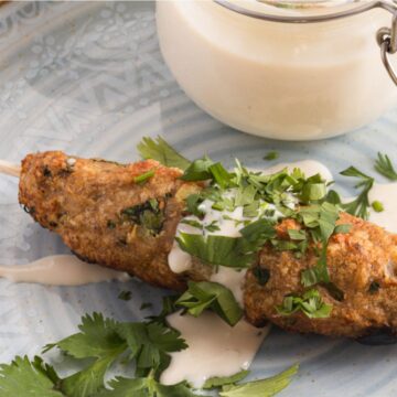 Grilled Grandma's Chicken skewers garnished with fresh herbs and served with a side of creamy sauce on a decorative blue plate.