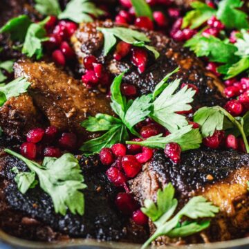 A close-up image of a slow-cooked meat dish garnished with fresh parsley and pomegranate seeds served in a rustic pot.