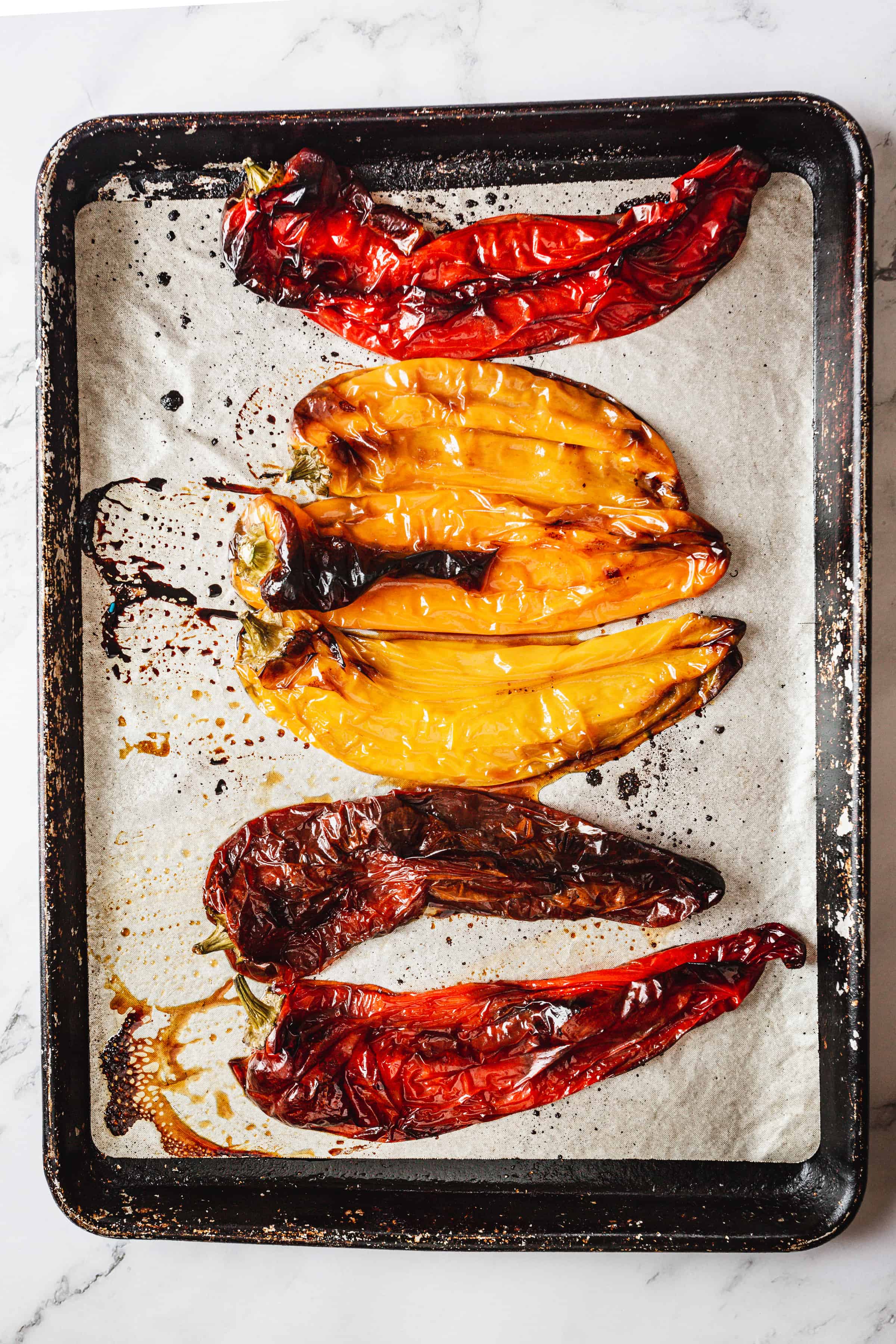 Roasted yellow and red bell peppers on a baking sheet covered with parchment paper, showing charred skins and released juices for a bell pepper bisque.